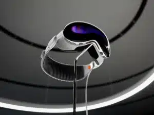 A sleek, futuristic virtual reality headset with a reflective visor, white straps, and a dark oval display, mounted on a stand with a circular ceiling light in the background.