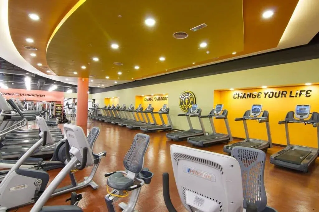 A modern gym interior featuring rows of treadmills and exercise bikes, with motivational phrases