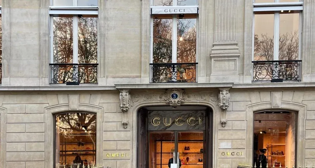 Exterior view of a Gucci store with large windows, ornate architectural details, and the brand name displayed above the entrance.