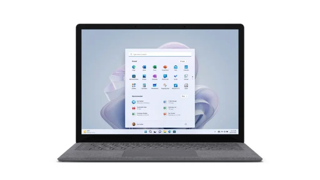 A laptop displaying the Windows 11 start menu on the screen, set against a plain background. The start menu shows various app icons arranged in a grid, with a search bar at the top.