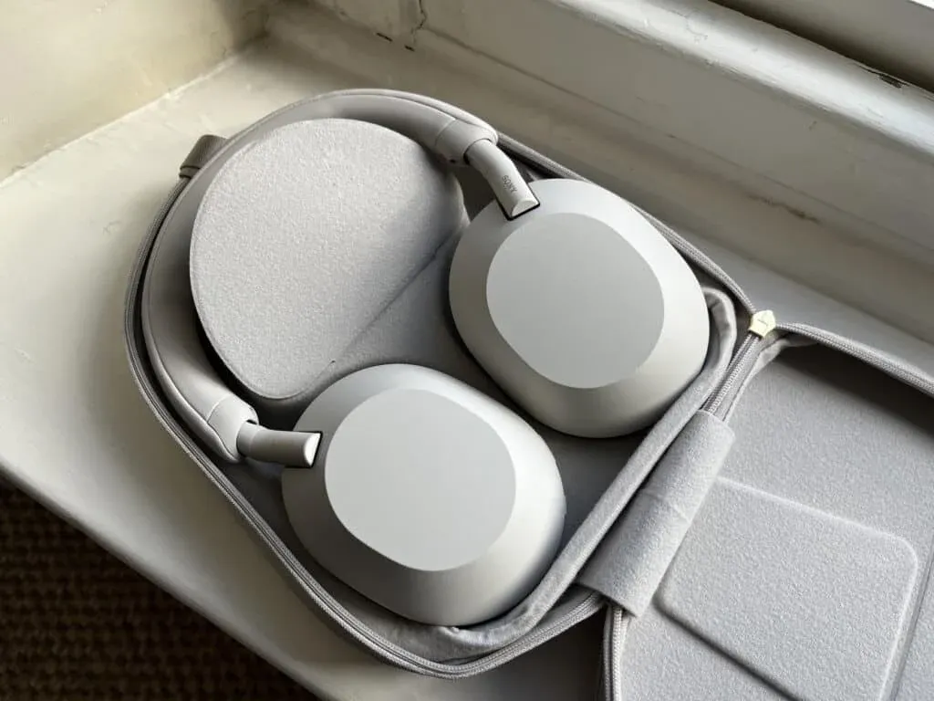 A pair of sleek, modern, over-ear headphones in a light grey color, neatly placed in an open carrying case with a soft, fabric interior.