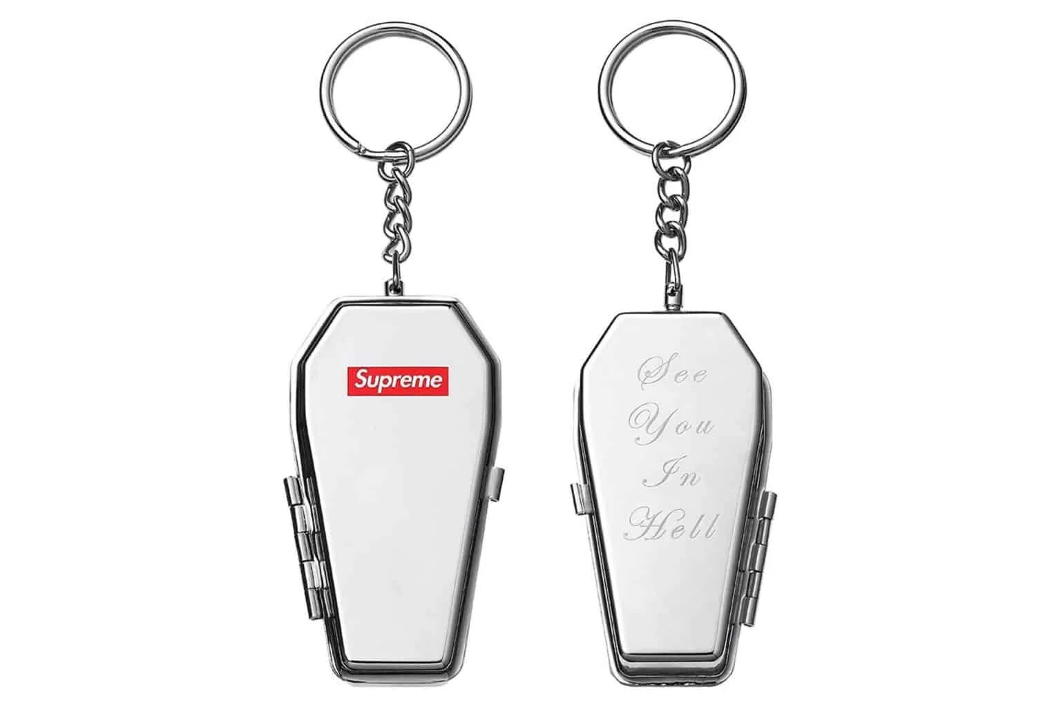 Two silver coffin-shaped keychains with hinged lids; one features a red logo, while the other is engraved with 'See You In Hell.'