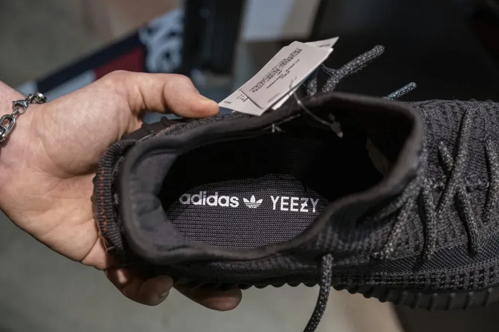 A hand holding a black Adidas Yeezy shoe, showing the inside with Adidas and Yeezy branding on the insole.