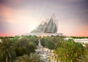 A futuristic architectural building with a series of curved, mesh-like structures towering over a landscaped garden with palm trees and people walking. The sky is lit with the warm colors of a sunset.