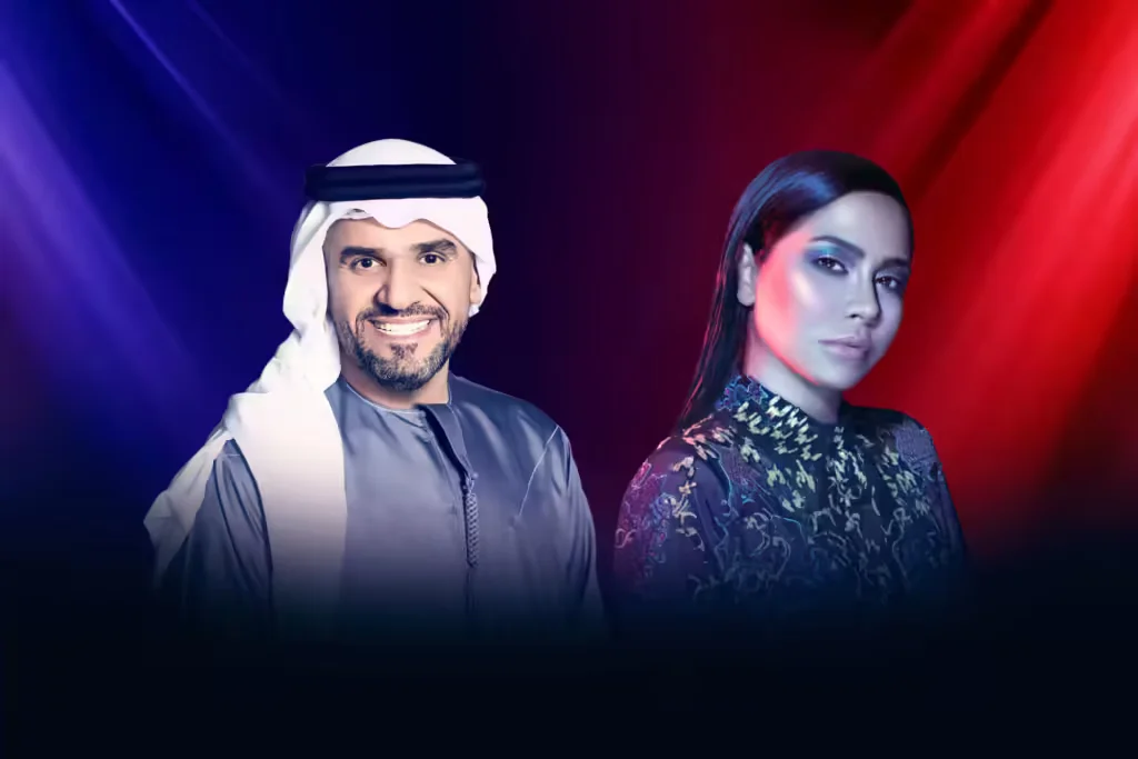A man wearing a traditional white headscarf and blue thobe stands next to a woman with sleek dark hair, wearing a detailed black patterned outfit, against a gradient background of purple and red hues.