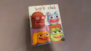 Cover of a publication titled "boy's club," featuring four cartoon characters with exaggerated facial features, including a furry character with sunglasses, a blue bear-like figure, a yellow dog-like figure, and a green frog-like figure.