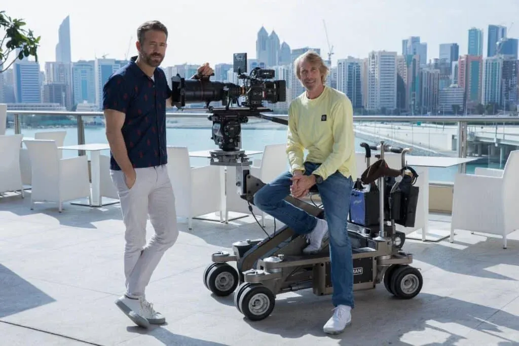 Two men on a terrace with a camera dolly and a city skyline in the background.