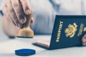 A person's hand holding a wooden stamp and a passport with a blue cover, prepared to stamp a document.