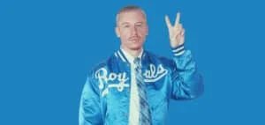 A person wearing a shiny blue jacket with the word 'Royals' printed in white, holding up a peace sign against a solid blue background.