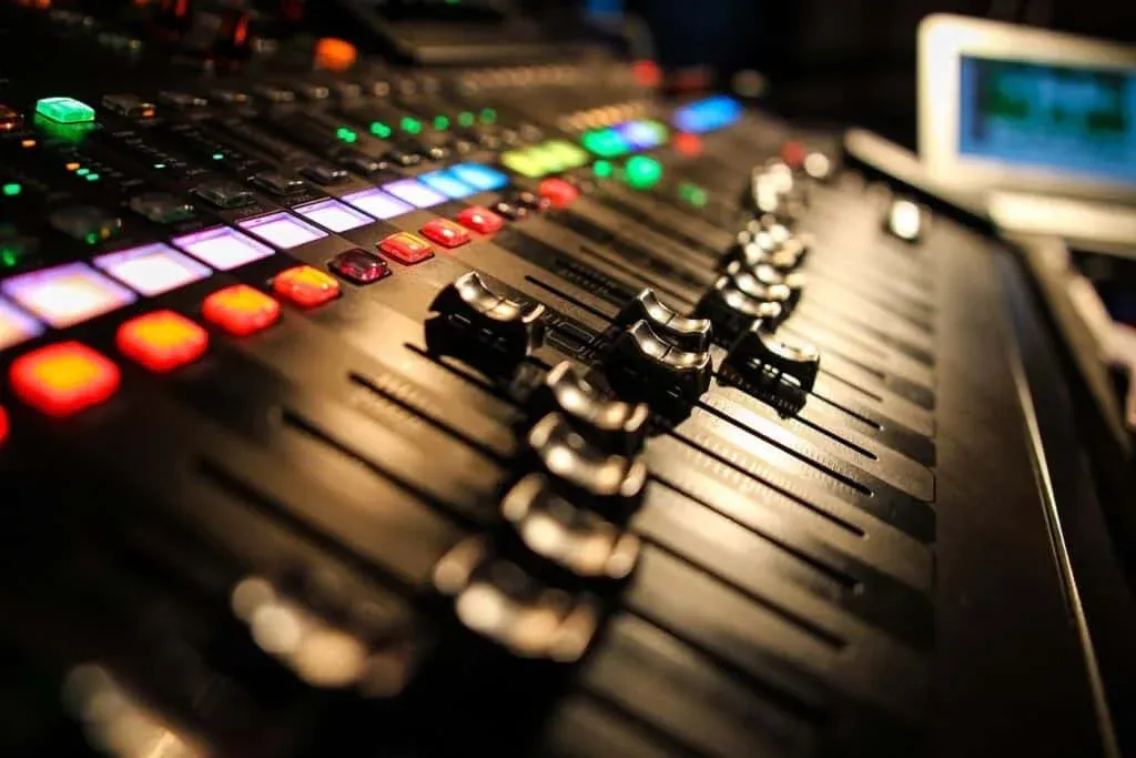 A close-up view of an audio mixing console with various colored buttons and sliders illuminated, suggesting a vibrant studio environment.