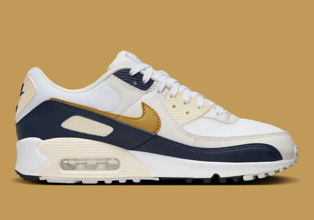 A white and navy sneaker with a gold swoosh logo, featuring a visible air unit in the sole, displayed on a tan background.