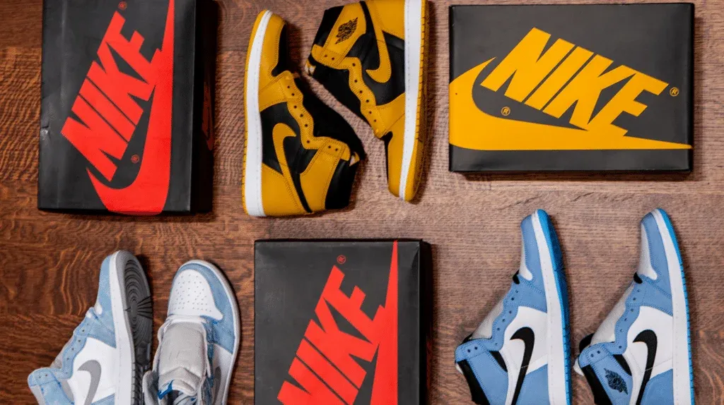 Two pairs of Nike Air Jordan sneakers displayed on a wooden floor, with one pair in blue and white and another in yellow and black, each next to their corresponding shoe boxes.