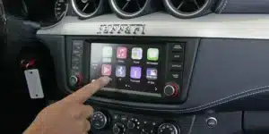A hand touches the display of a car's infotainment system featuring various app icons, with the brand name 'Ferrari' above it.
