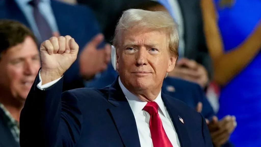 A person in a suit and red tie raises their fist in front of a crowd.
