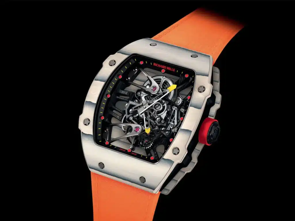 A luxury watch with an intricate open-worked dial, a silver case with exposed screws, and an orange strap. The watch features prominent, visible gears and mechanical components, with yellow and black hands. The crown is detailed with a red accent.