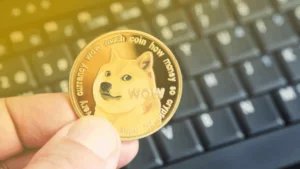 A person holding a Dogecoin, featuring the Shiba Inu meme dog, in front of a computer keyboard.