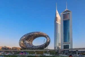 The Museum of the Future, a torus-shaped building with Arabic inscriptions, adjacent to twin skyscrapers in a modern cityscape under a clear blue sky.