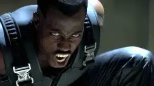 A fierce-looking man with fangs, wearing a black tactical outfit, appears to be snarling intensely.
