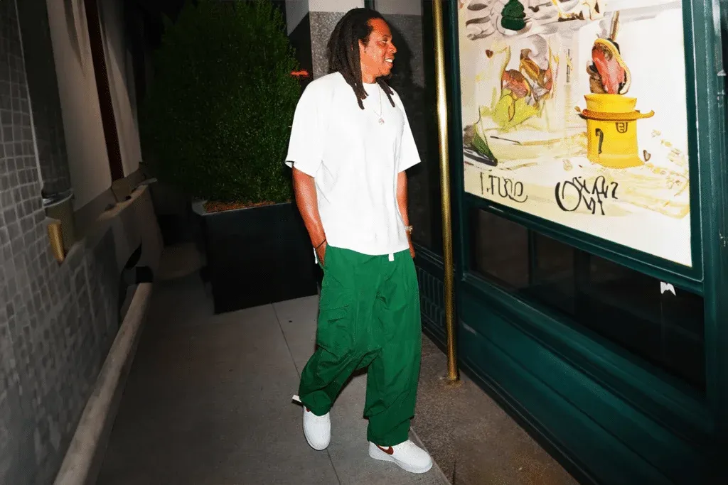A person walking in an urban setting, wearing a white T-shirt, green pants, and white sneakers.