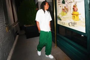 A person walking in an urban setting, wearing a white T-shirt, green pants, and white sneakers.