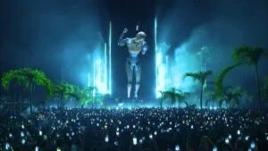 A large crowd at a nighttime outdoor concert, with many people holding up glowing smartphones. A gigantic, illuminated robot figure towers over the crowd, with palm trees visible on either side of the scene.