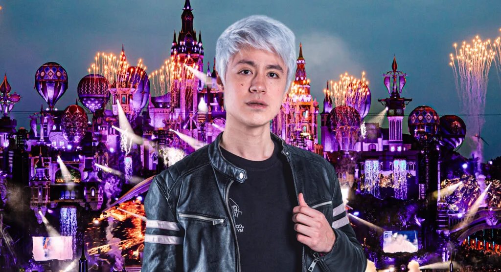 A person with silver hair wearing a black leather jacket stands in front of a colorful, illuminated fantasy-themed backdrop featuring castles and towers, with fireworks lighting up the sky.