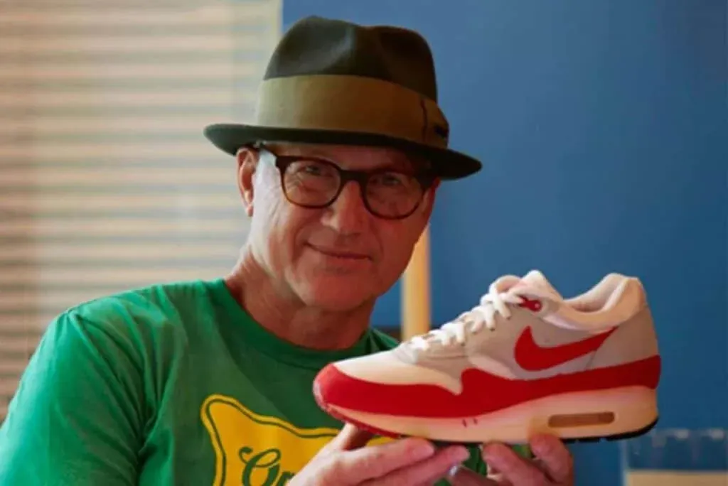 A person wearing glasses and a hat holds a red and white sneaker with a Nike logo.