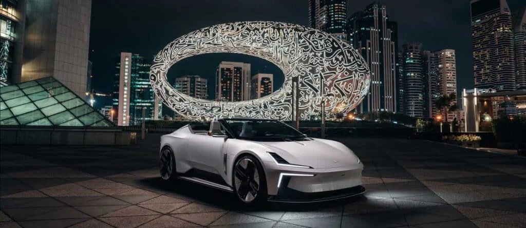 A sleek white sports car parked in front of a futuristic oval building with illuminated Arabic calligraphy at night, surrounded by towering skyscrapers.