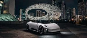 A sleek white sports car parked in front of a futuristic oval building with illuminated Arabic calligraphy at night, surrounded by towering skyscrapers.