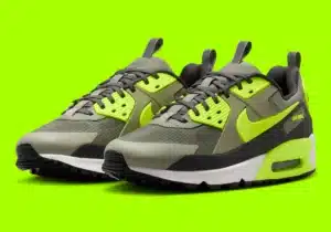 A pair of athletic shoes with a gray, black, and neon green color scheme, featuring a prominent Nike logo on the side. They are set against a bright green background, highlighting the vibrant design of the sneakers.