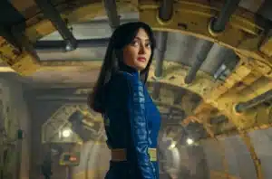 A person wearing a blue outfit stands in a futuristic, tunnel-like setting with yellow archways and exposed pipes.