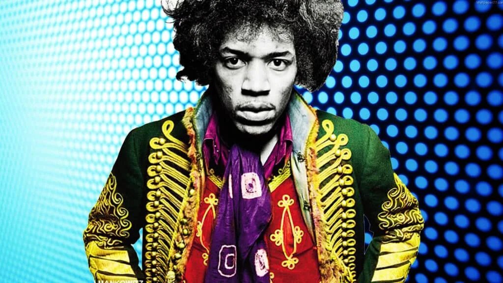 A person with a serious expression, wearing a colorful military-style jacket and scarf, in front of a blue dotted background.