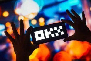 Silhouette of a hand holding a smartphone displaying the logo 'OKX' against a colorful, blurred background with bokeh lights.
