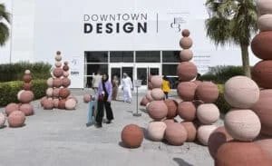 Visitors walking outside a building marked 'Downtown Design' with stacks of red and pink spherical sculptures arranged in clusters around the area.