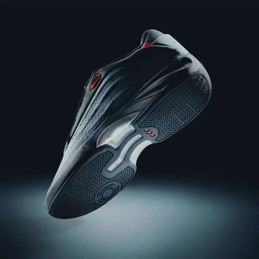 A dark-colored sneaker shown from the side and bottom, highlighting its textured sole and streamlined design, with subtle red accents.