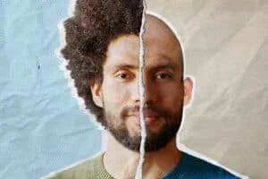 Composite image of a man's face split in half; the left side features an afro hairstyle and a green sweater, while the right side is bald with a blue sweater, with a textured, torn-paper effect along the divide.