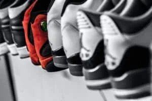 Close-up of a row of sneakers placed side by side, with a focus on a red sneaker featuring a prominent green eye-like detail on the side, surrounded by mostly black and white shoes.