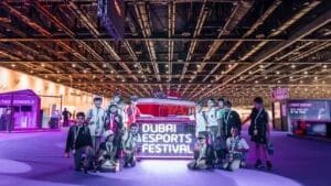 A group of children pose in front of a sign reading 'Dubai Esports Festival' inside a large, well-lit indoor venue. They appear to be excited and are dressed in casual and sporty attire, surrounded by displays and booths related to esports.