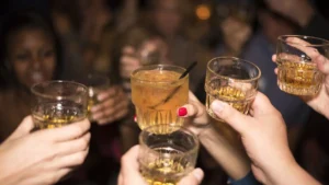 A group of people clinking their glasses filled with a golden-brown beverage in a celebratory manner.