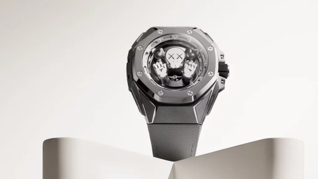 A luxury watch with a metallic gray case and a unique dial featuring a stylized character's face with crossed eyes and raised hands. The watch is displayed on a curved stand against a light background.