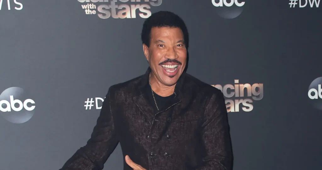 A person smiling widely at a 'Dancing with the Stars' event, standing in front of a backdrop featuring the show's logo and ABC logo.