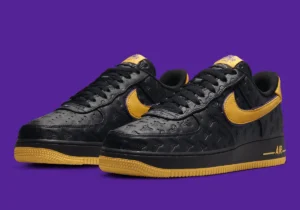 A pair of black sneakers with embossed designs, featuring yellow swooshes and soles, set against a purple background.