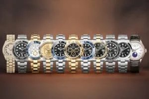 A lineup of nine luxury watches with various designs and metal bands, including gold, silver, and diamond-encrusted components, displayed against a brown gradient background.