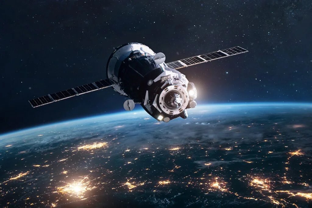 Satellite orbiting Earth with city lights visible on the planet's surface and a starry sky in the background.