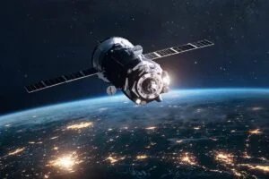 Satellite orbiting Earth with city lights visible on the planet's surface and a starry sky in the background.