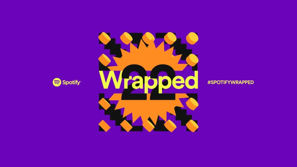 A promotional graphic for Spotify Wrapped 22 on a purple background, featuring the word 'Wrapped' over a vibrant orange and yellow design with the number '22' and yellow geometric shapes. The Spotify logo and hashtag #SPOTIFYWRAPPED are also displayed.
