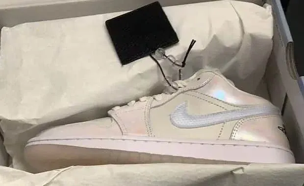 A single pearl-colored sneaker with a reflective Nike swoosh displayed in a shoebox lined with white paper.