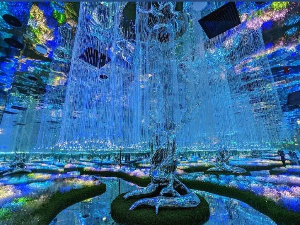 Futuristic art installation with mirrored ceilings and floors, featuring glowing fiber-optic trees and paths of illuminated greenery.