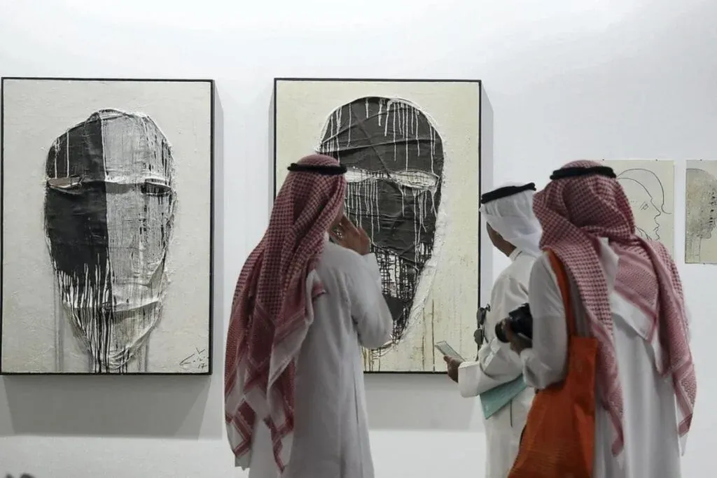Group of people in traditional attire viewing abstract paintings in an art gallery.