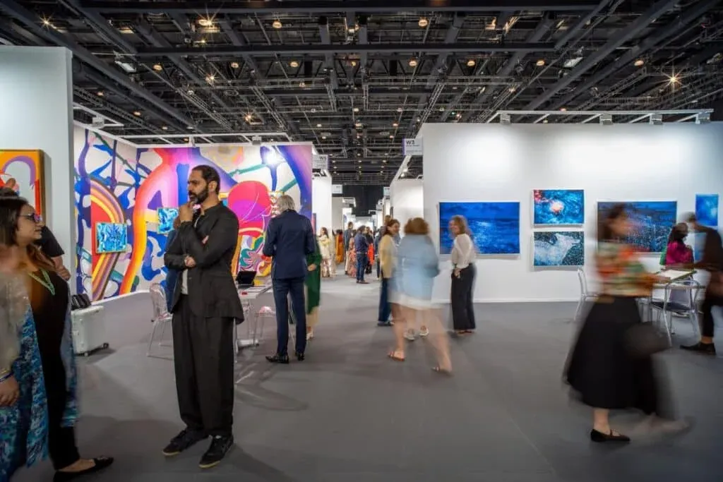 People walking in an art gallery with colorful abstract paintings displayed on white walls.
